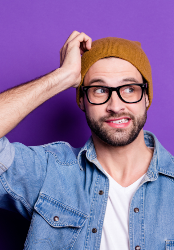 Man with glasses and beanie has hand on head as he thinks