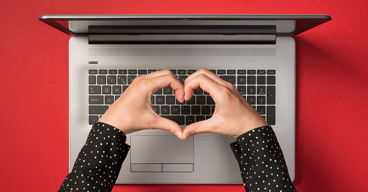 Hands making a heart shape over a laptop keyboard